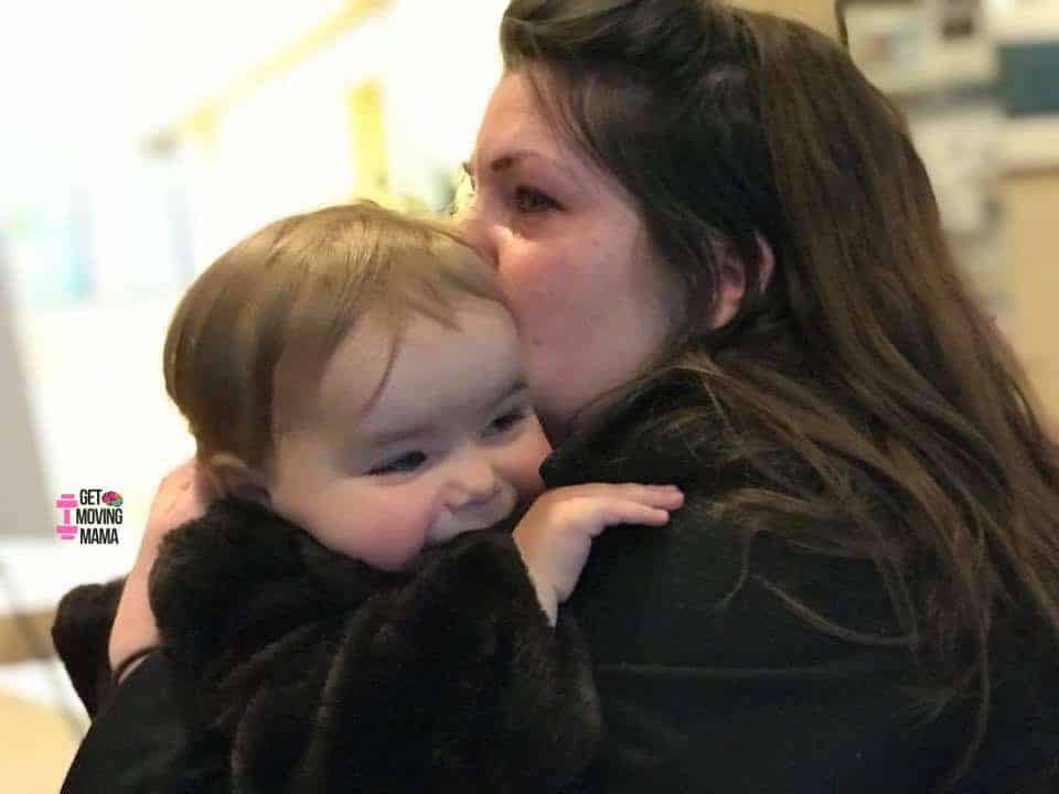 A mom hugging a toddler while teary eyed.