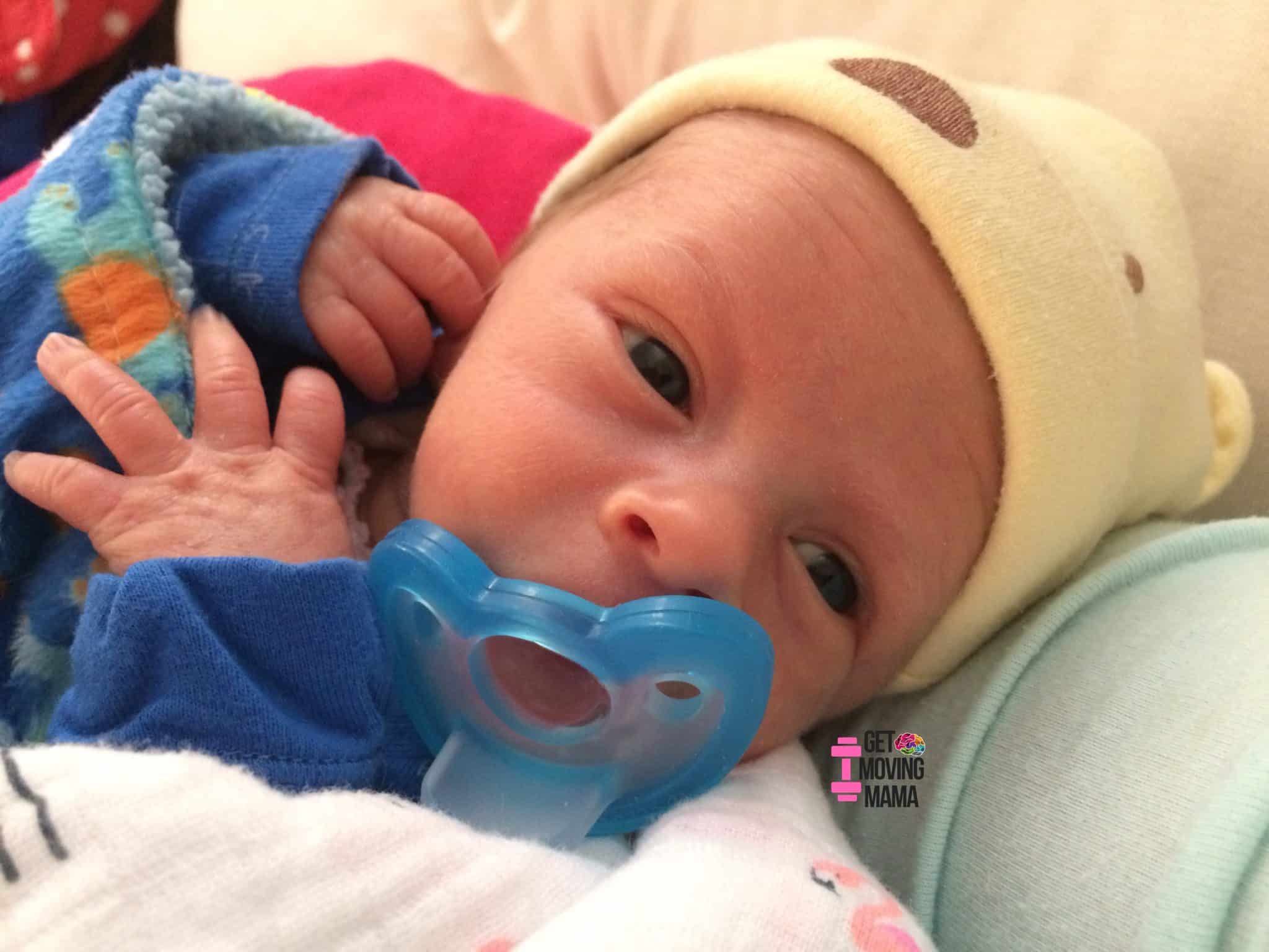 A baby boy snuggling with a blue pacifier in his mouth.