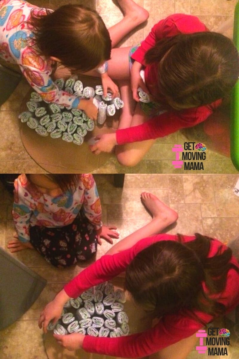 A picture of two girls making the bottom layer of a diaper cake for a baby shower gift.