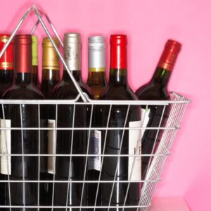 A picture of wine bottles in a metal basket with a pink background.