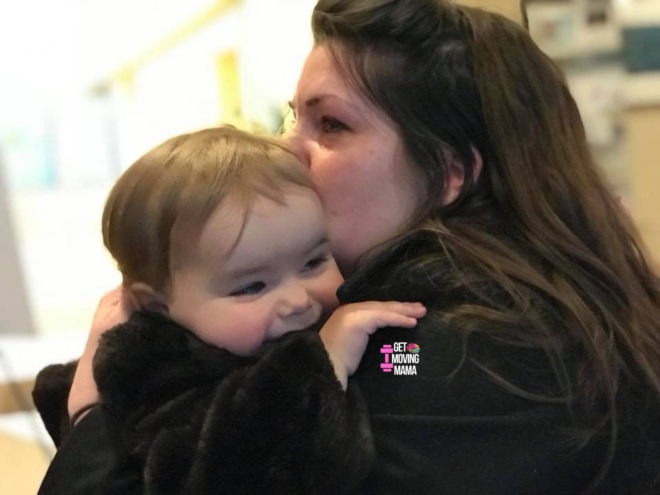 A postpartum mom snuggling a toddler with tears in her eyes.